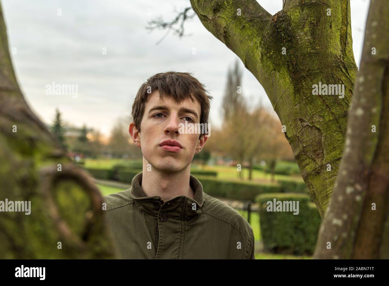 A pensive young man standing among trees looks out with an air of melancholy. Stock Photo