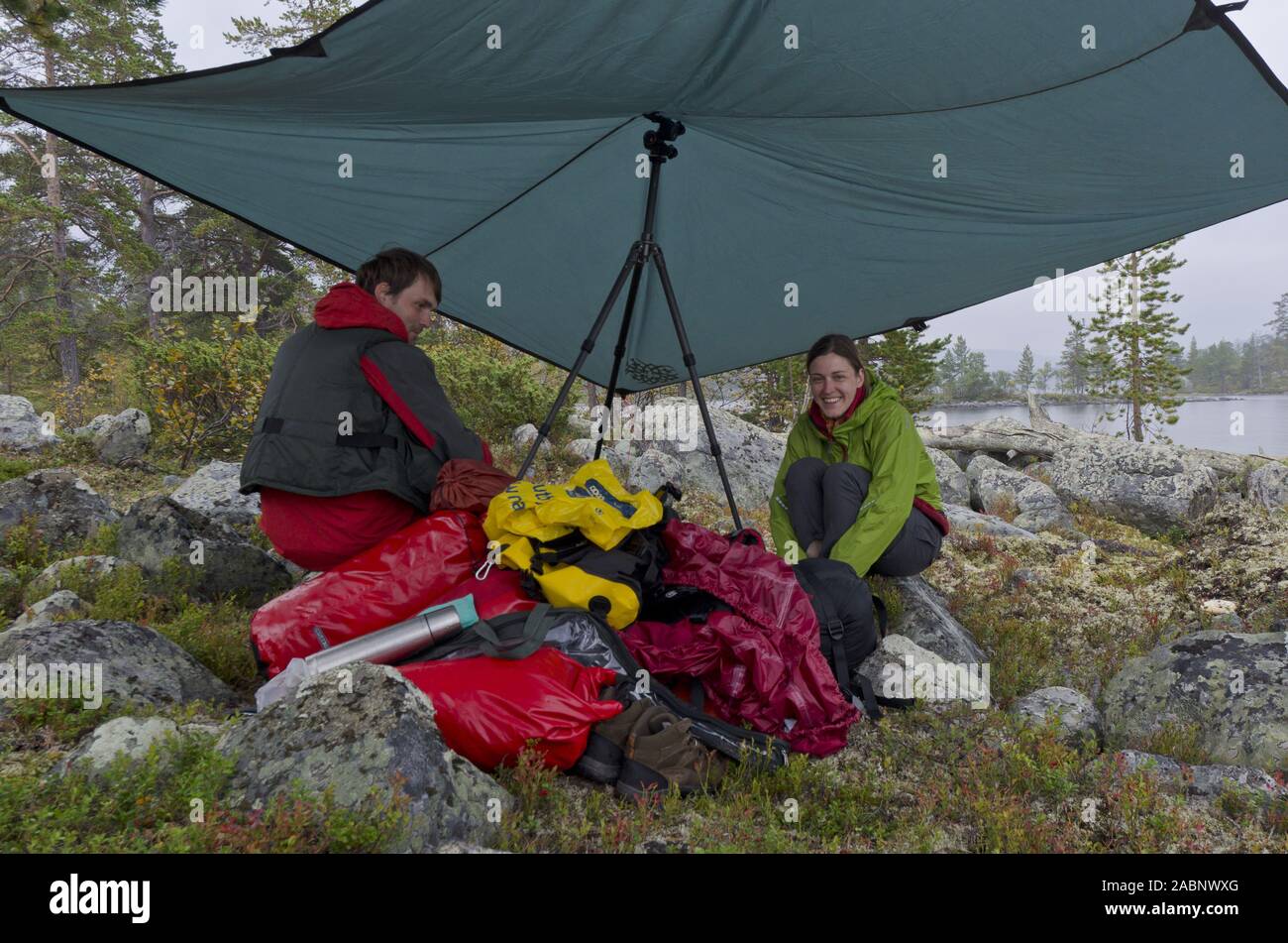 Paar sitzt im Regen unter einer Zeltplane (Tarp) am See Rogen, Naturreservat Rogen, Haerjedalen, Schweden, August 2011 Stock Photo