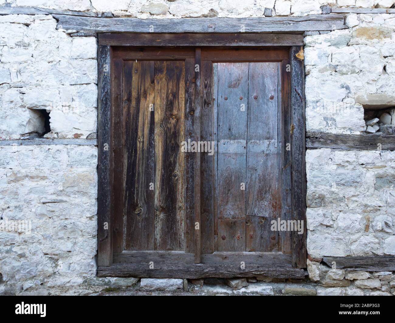 Weathered wooden door with wood beams between layers of stone in an old building. Stock Photo