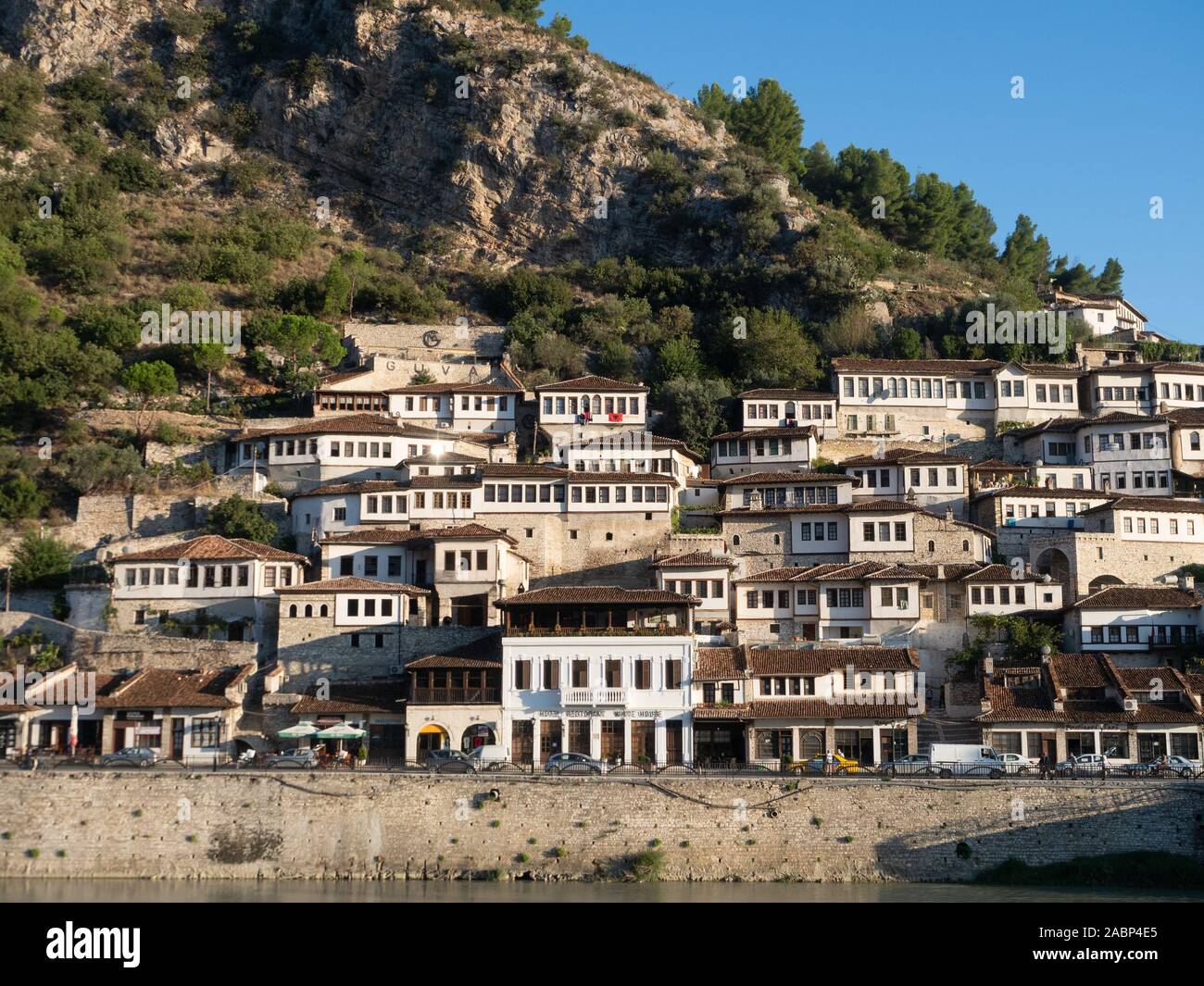 Berat, Albania - September 27, 2019: Ottoman houses with multiple windows built on a hillside in Berat, Albania with the River Osum and businesses in Stock Photo