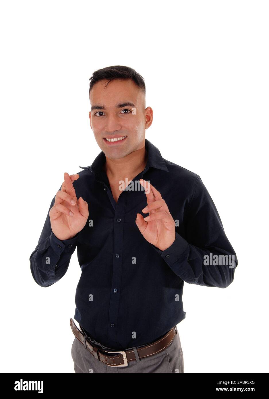 A young East Indian man standing in a black shirt in the studio, crossing his fingers to have luck, isolated over white background Stock Photo