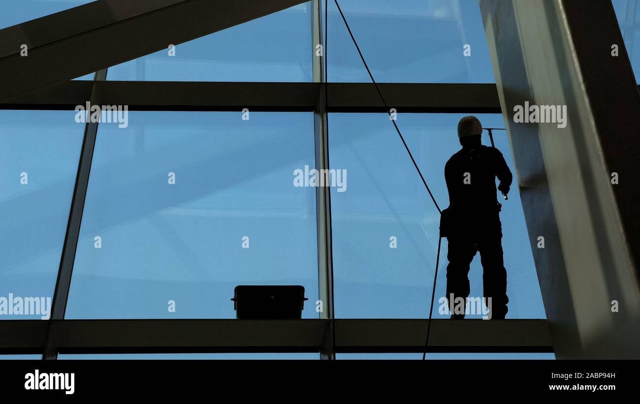 Worker man is washing windows with scraper on a highrise modern ...