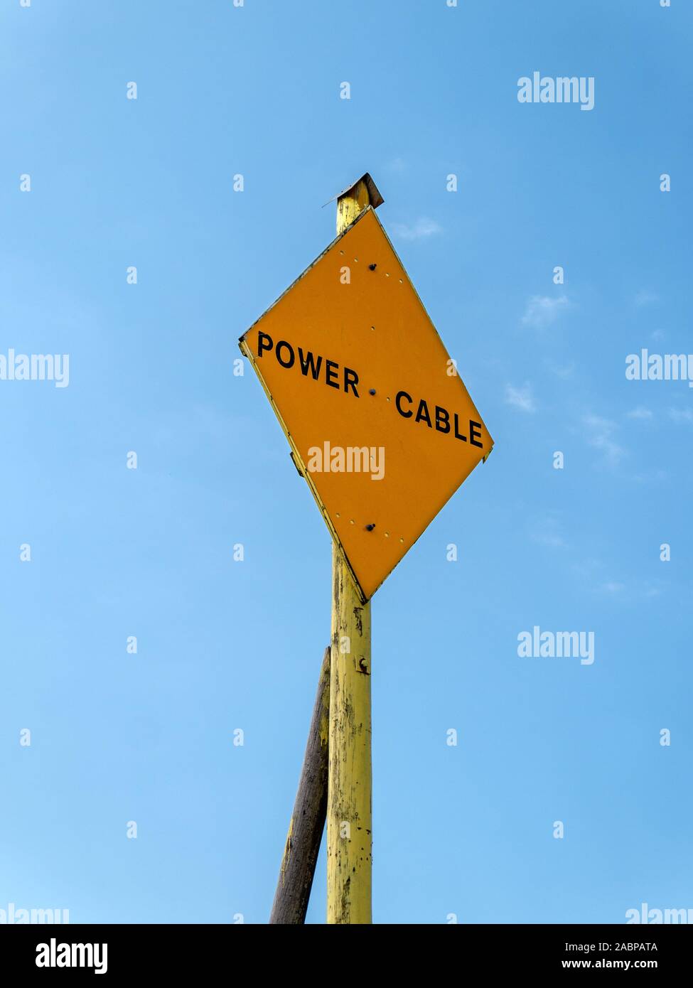 Yellow diamond shaped undersea power cable warning sign against blue sky, Isle of Colonsay, Scotland, UK Stock Photo