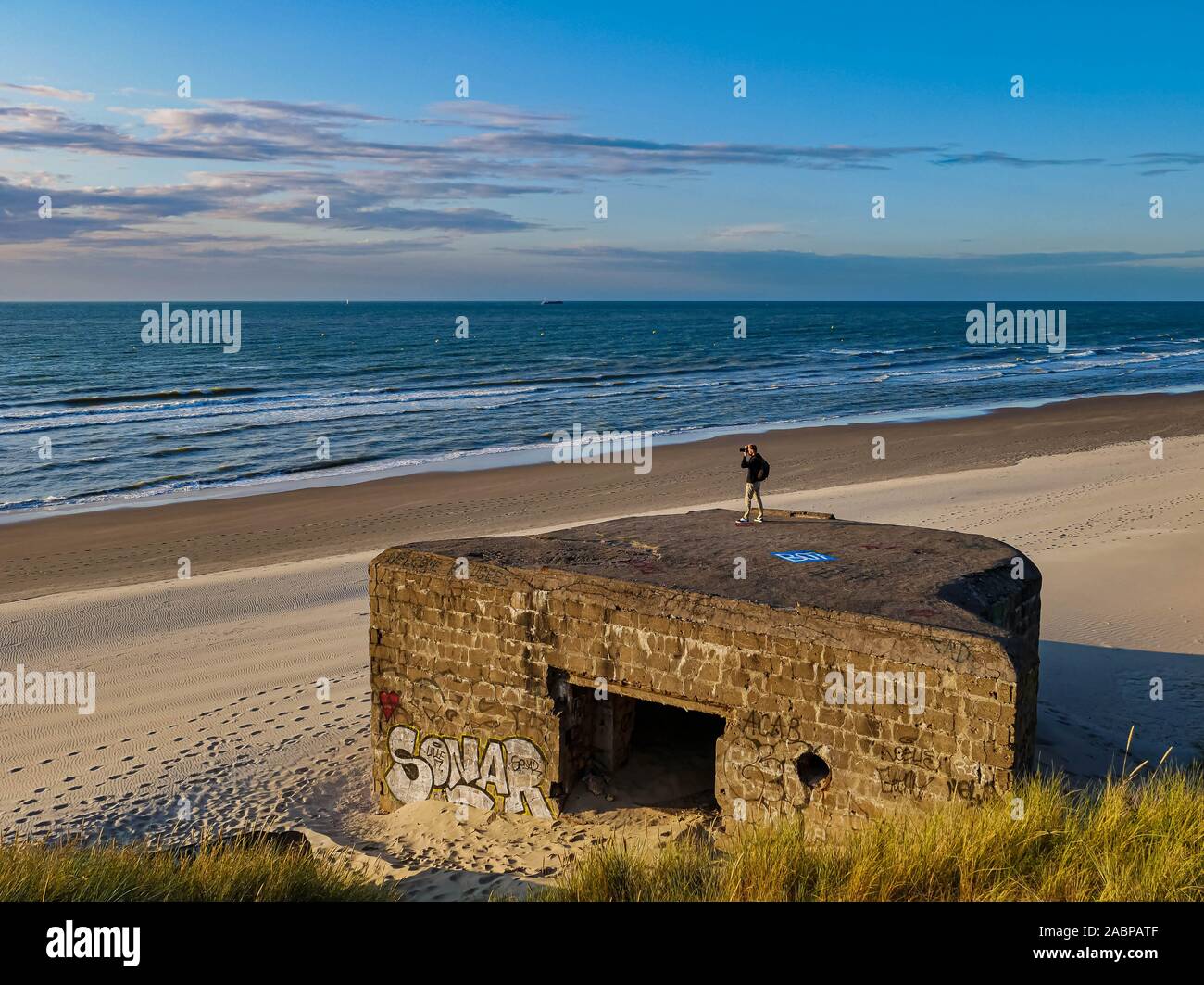 Young man taking pictures from remains of a WW2 bunker with graffiti at a French beach Stock Photo
