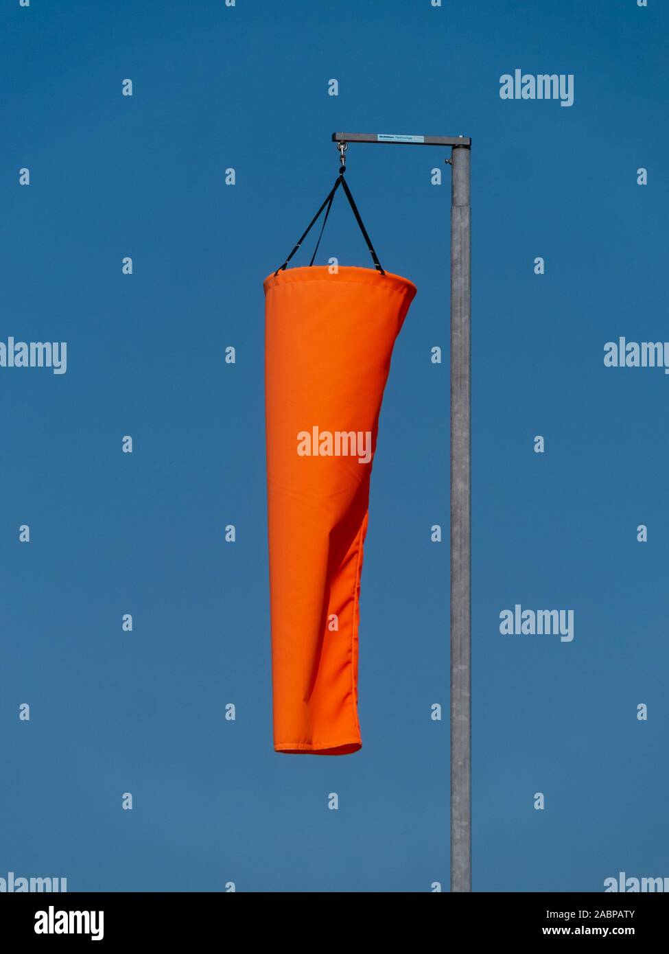 Bright new orange windsock hanging down in calm, still weather with no wind and blue sky behind. Stock Photo