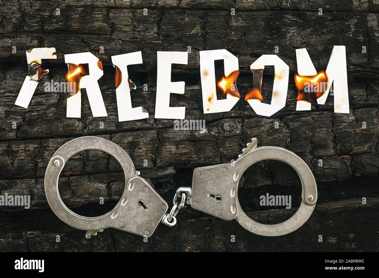 The word freedom burns on coals, and handcuffs lie nearby. Burning letters made of paper. Justice concept Stock Photo