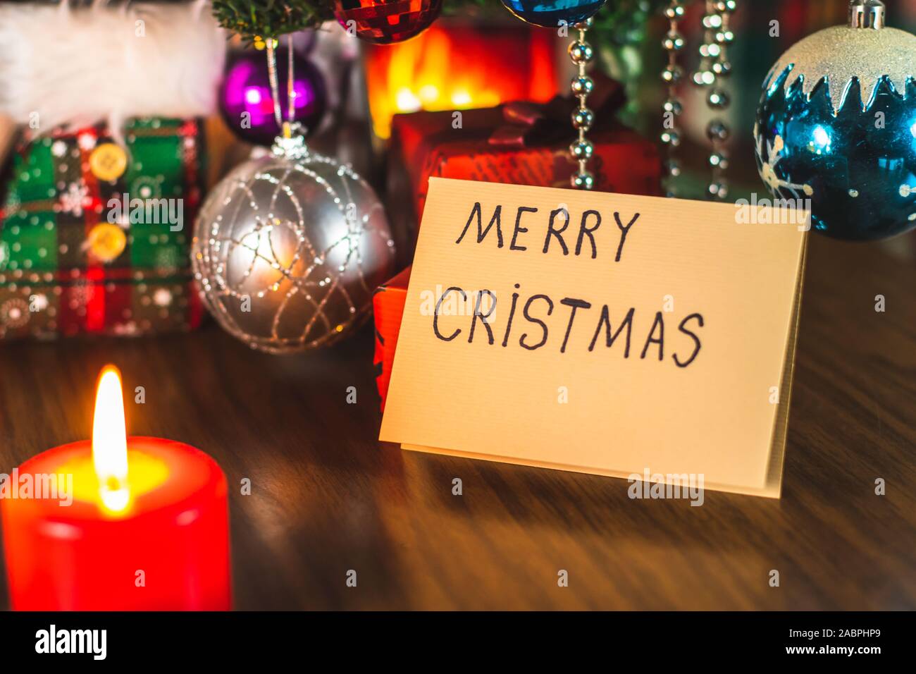 Merry Christmas written on a greeting card under a Christmas tree with decorations and ornaments. Festive celebration. Stock Photo