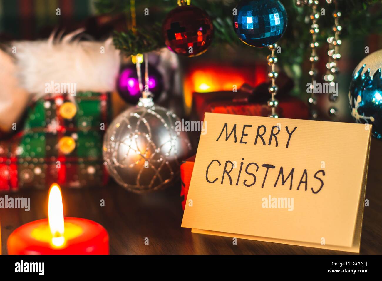Merry Christmas written on a greeting card under a Christmas tree with decorations and ornaments. Festive celebration. Stock Photo