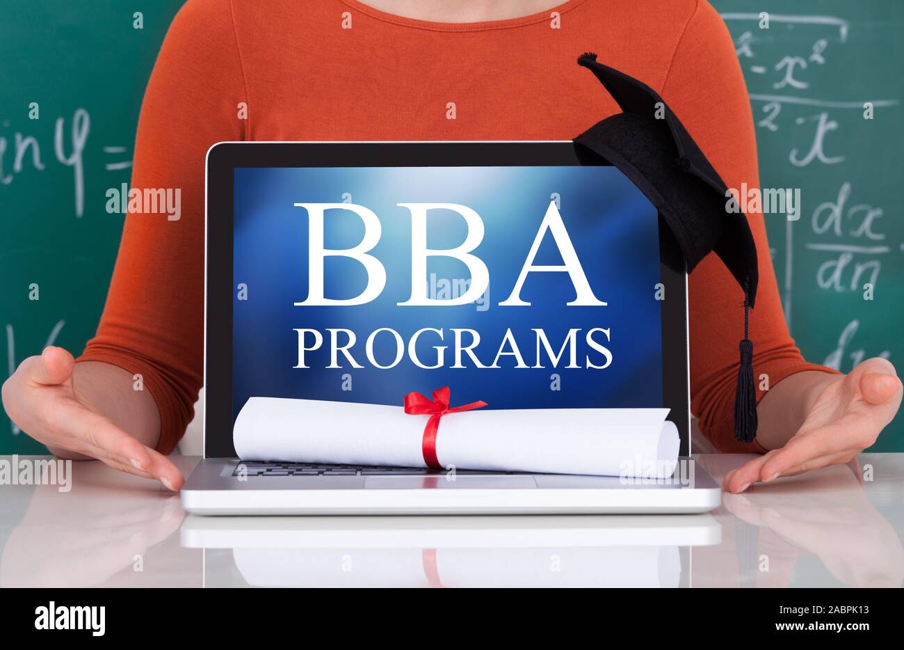 Woman Sitting Against Green Chalkboard With Bba Programs Text On Laptop Stock Photo