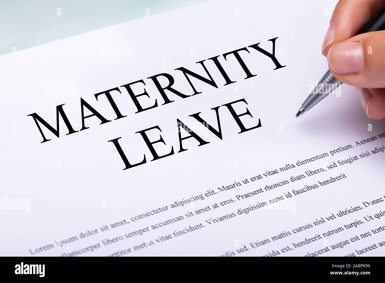 Close-up Of A Woman's Hand Filling Maternity Leave Form Holding Pen Over Desk Stock Photo
