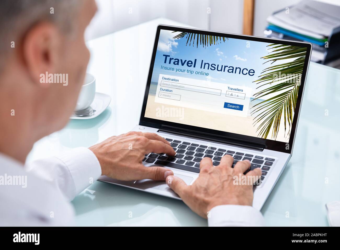 Man Sitting In Office Working On Laptop With Travel Insurance Application On Screen Stock Photo
