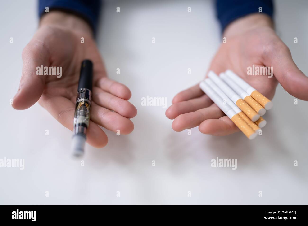 Man Holding Vape And Tobacco Cigarette Over Desk Stock Photo