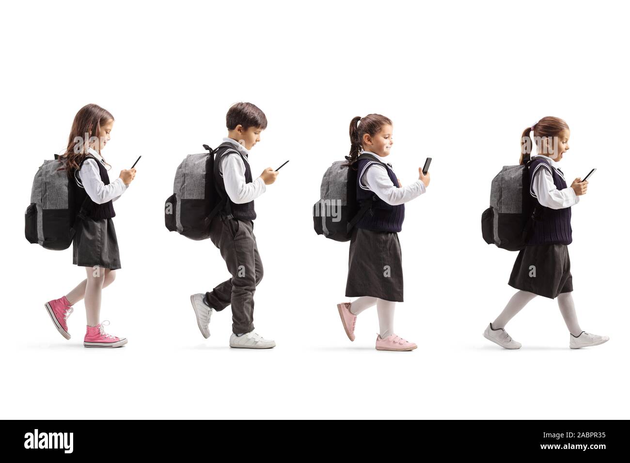 Full length profile shot of three schoolgirls and one schoolboy with mobile phones walking in line isolated on white background Stock Photo