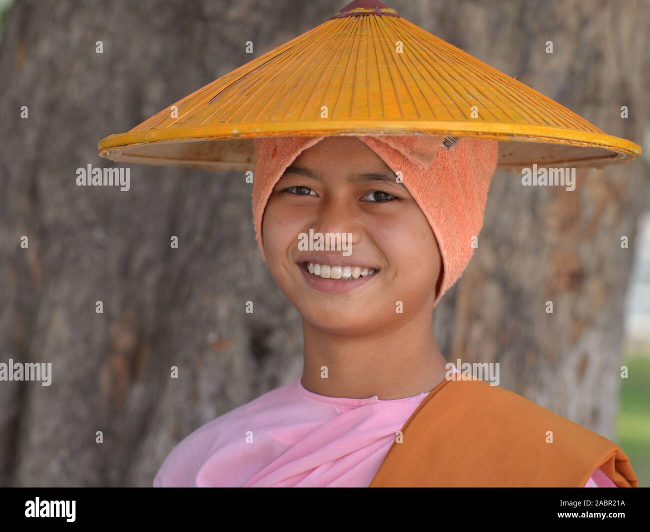 Burmese Buddhist nun covers her shaved head with a bath towel and an Asian conical hat. Stock Photo