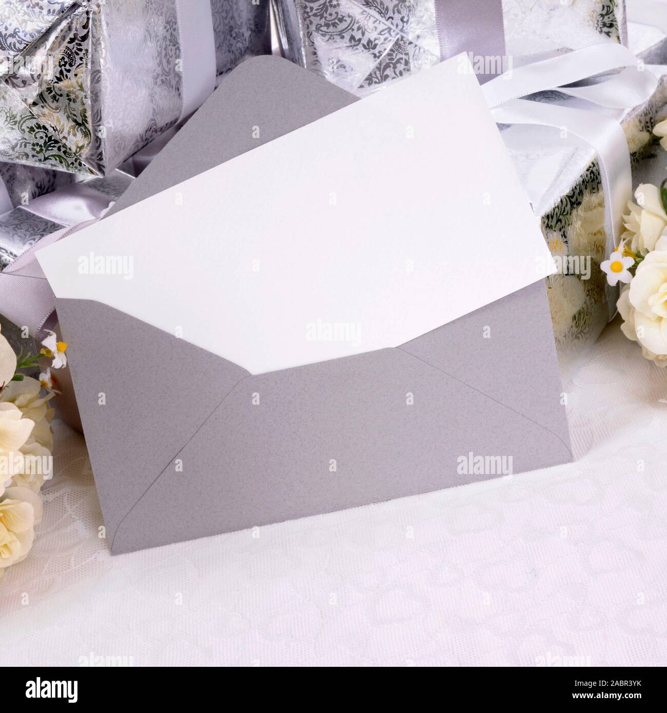 Blank invitation or thank you card with several wedding gifts and white rose bouquet laid on bridal lace.  Space for copy. Stock Photo