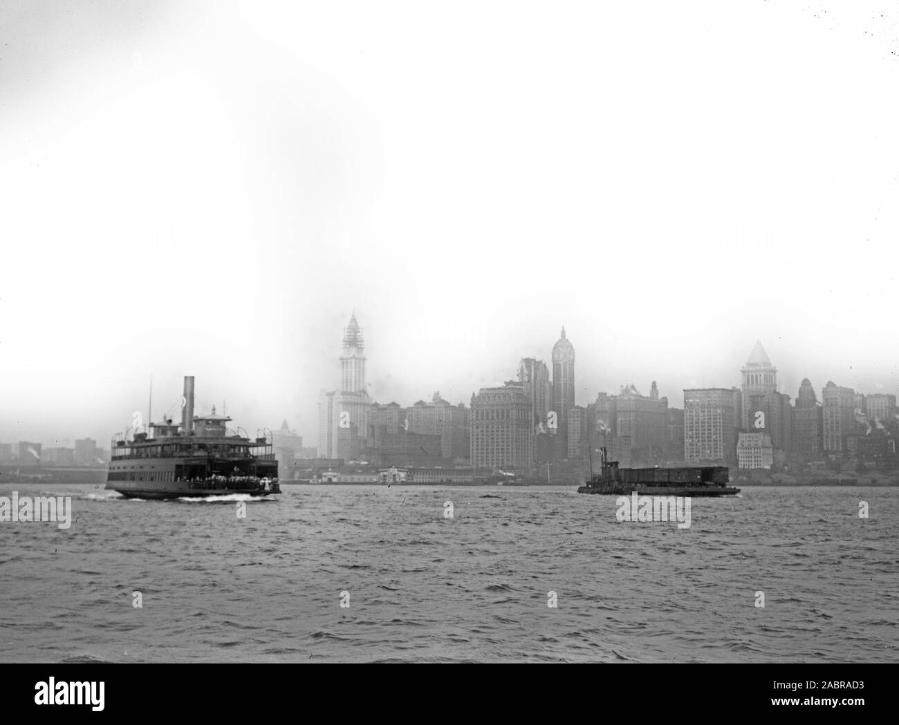 Photo shows Lower Manhattan, New York City, with ferry in foreground. Identified buildings include (from left): Woolworth Building (with tower nearing completion), Hudson Terminal, West Street Building, City Investing Tower, Singer Building, U.S. Realty and Trinity buildings, United States Express Company, Bankers Trust Tower, and 47 West Street Building. Stock Photo