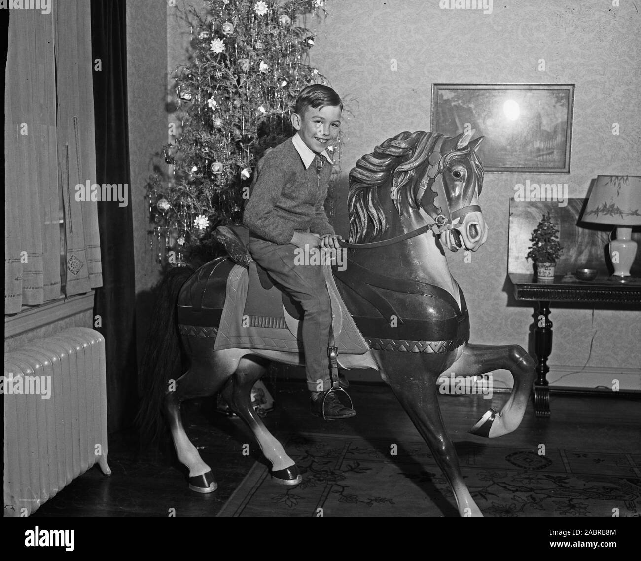 Boy riding a play horse inside living room near Christmas tree ca. 1935-1936 Stock Photo