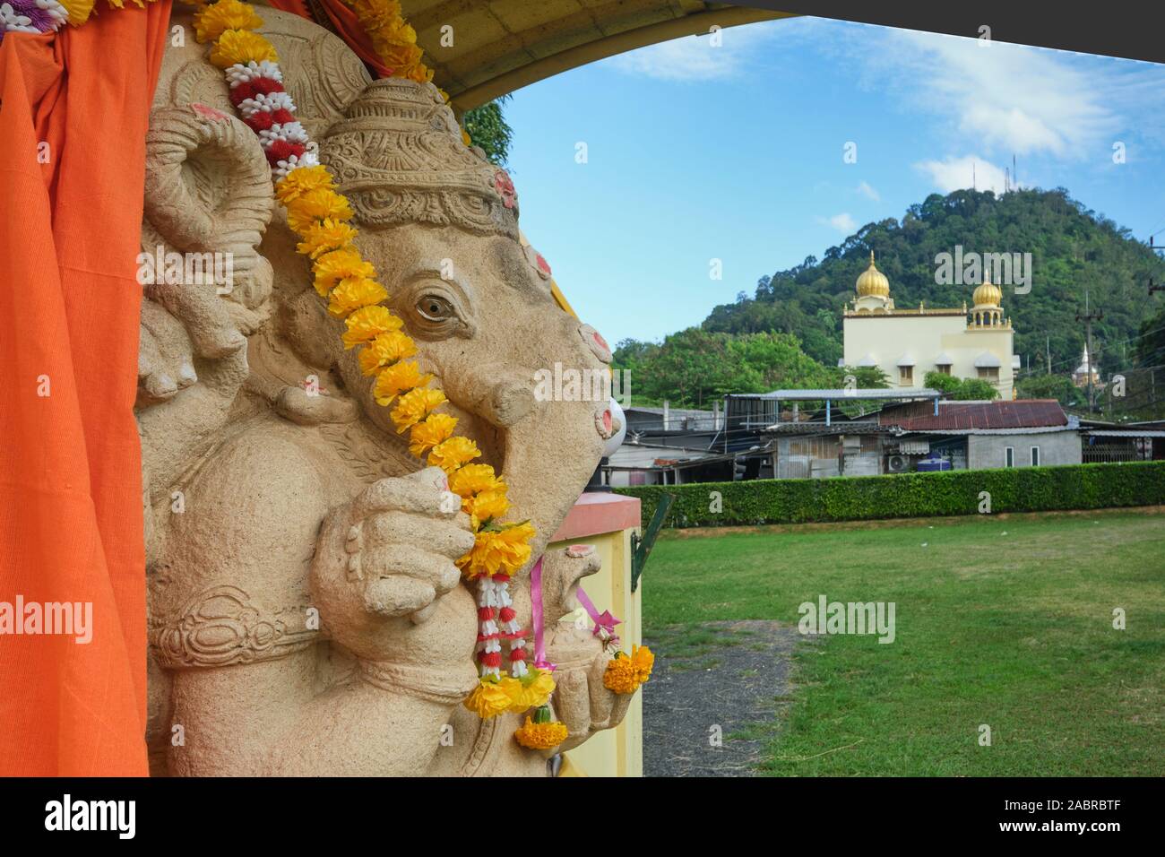 A statue of Hindu elephant god Ganesh at Thendayuthapani (Hindu) Temple in Phuket Town, Thailand; b/g: Gurdwara Siri Guru Singh Sabha (Sikh temple) Stock Photo