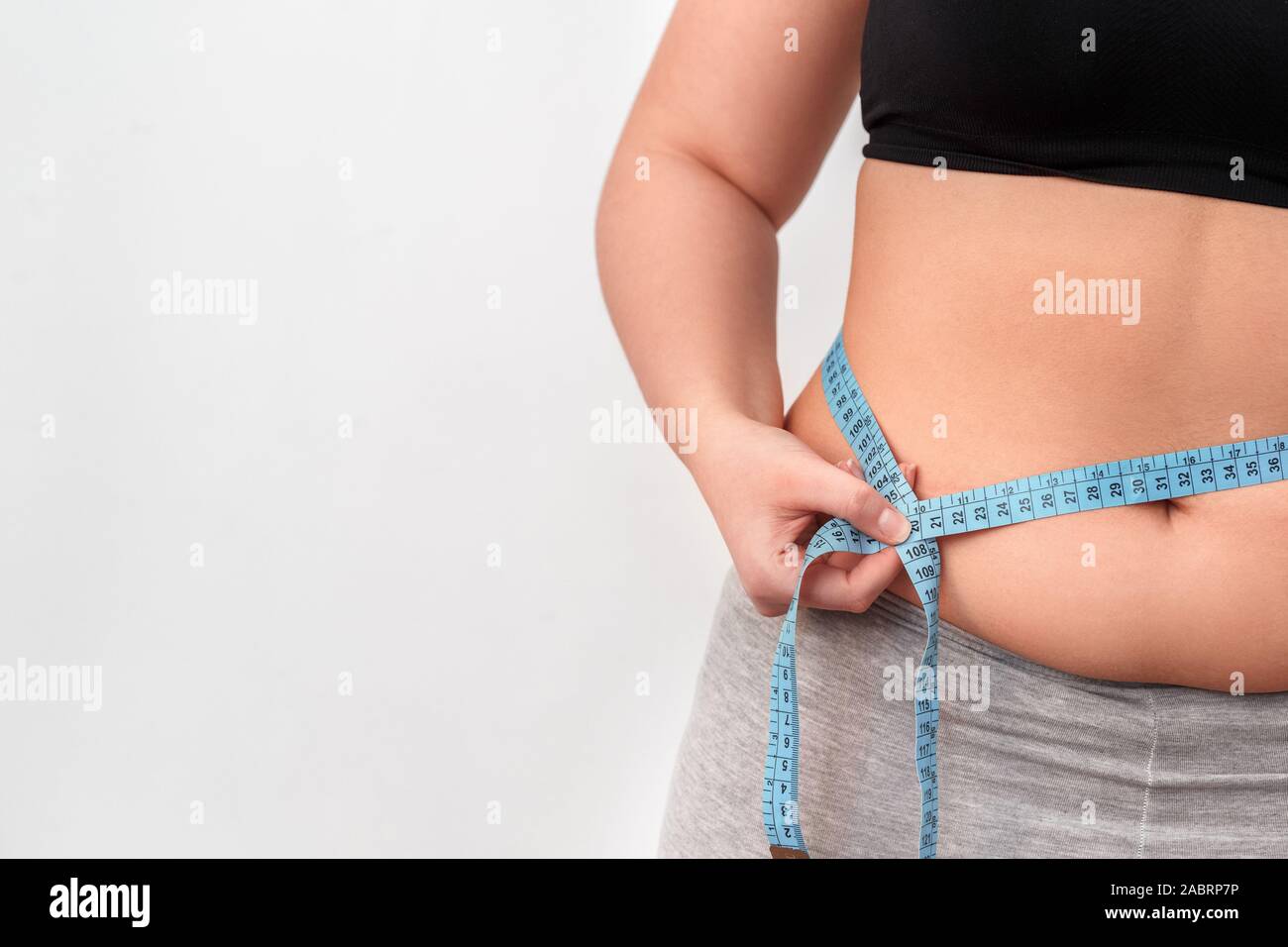 https://c8.alamy.com/comp/2ABRP7P/young-chubby-woman-with-bare-belly-standing-isolated-on-white-wall-holding-tape-measure-measuring-waist-close-up-half-body-shot-2ABRP7P.jpg