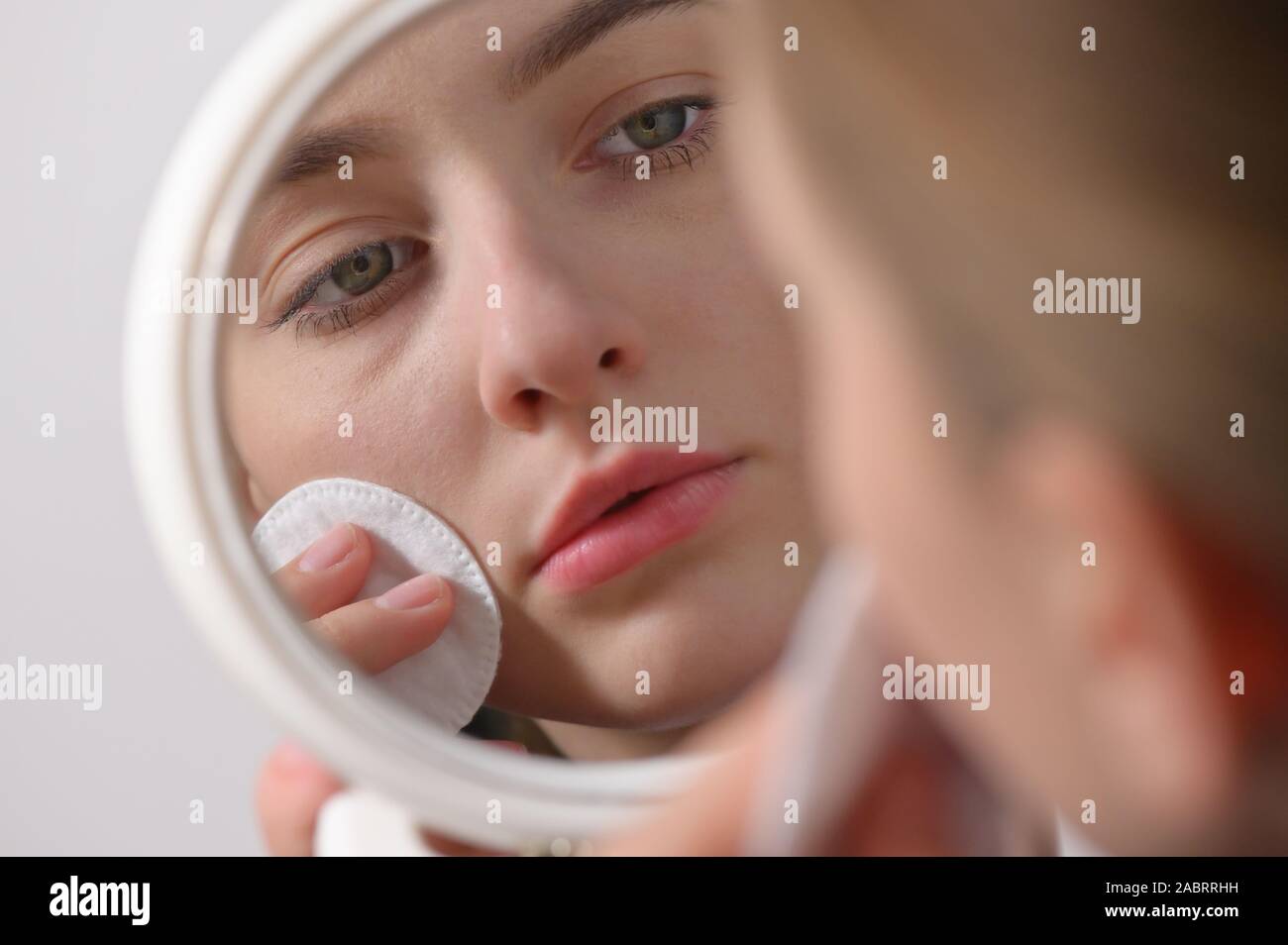 Girl Wipes Her Face With A Cotton Pad in Mirror Stock Photo