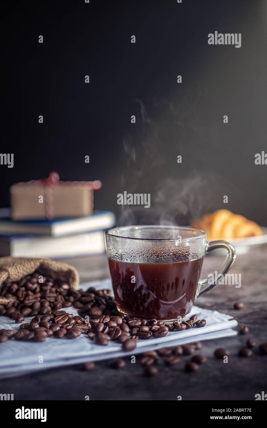 a cup of hot espresso coffee drink with smoke and roasted coffee beans on the table in the morning. vertical image, cropped shot Stock Photo