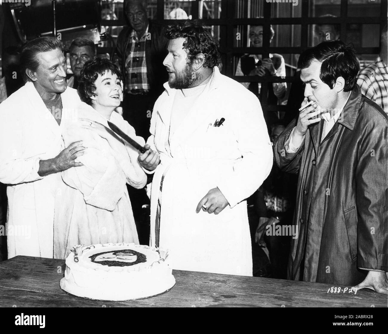 KIRK DOUGLAS JEAN SIMMONS and Director STANLEY KUBRICK watch PETER USTINOV cut his surprise birthday cake on set candid during filming of SPARTACUS 1960 novel Howard Fast screenplay Dalton Trumbo executive producer Kirk Douglas Bryna Productions / Universal Pictures Stock Photo