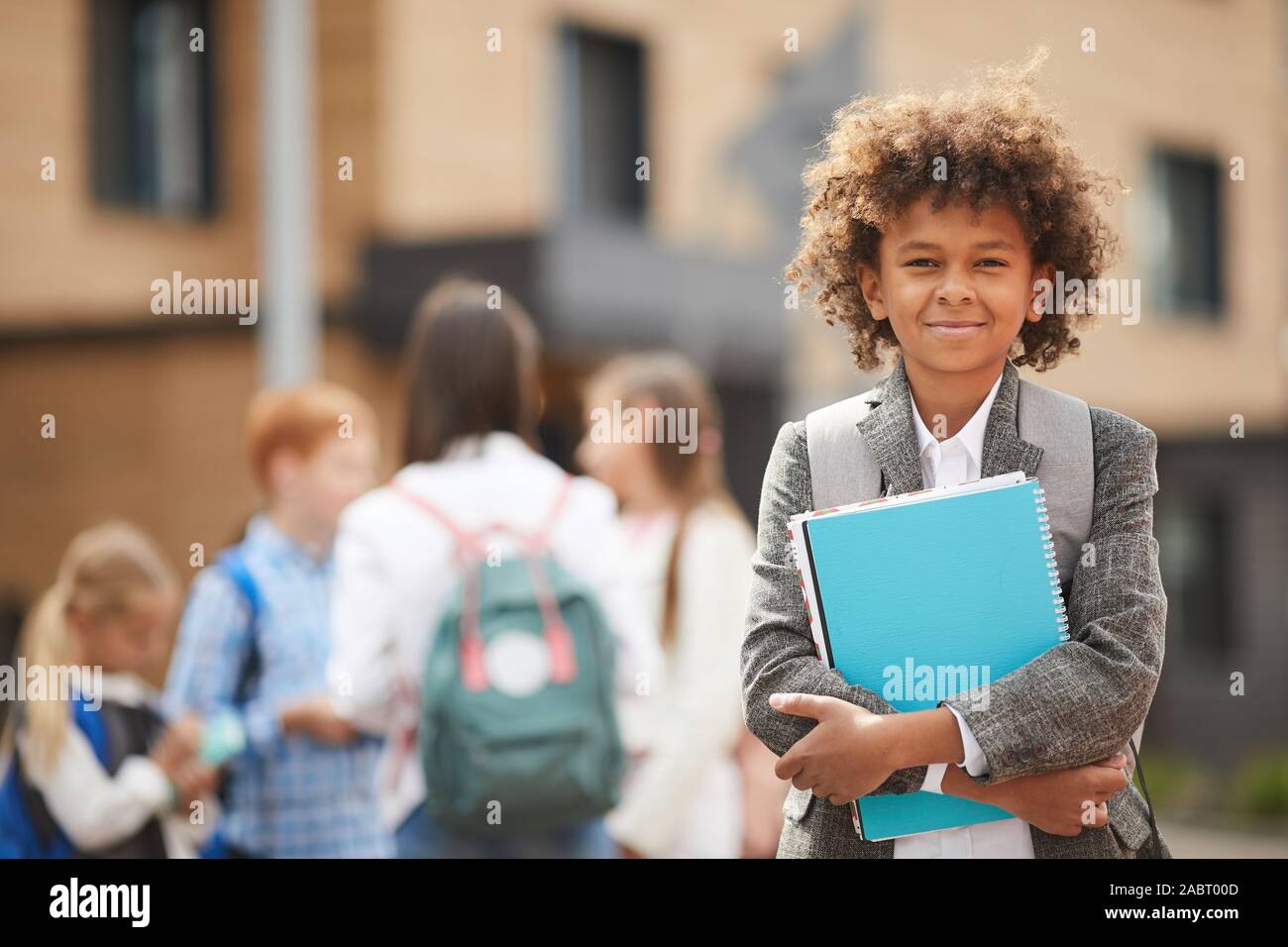 Portrait of African schoolboy with curly hair holding textbooks and smiling at camera while standing outdoors Stock Photo