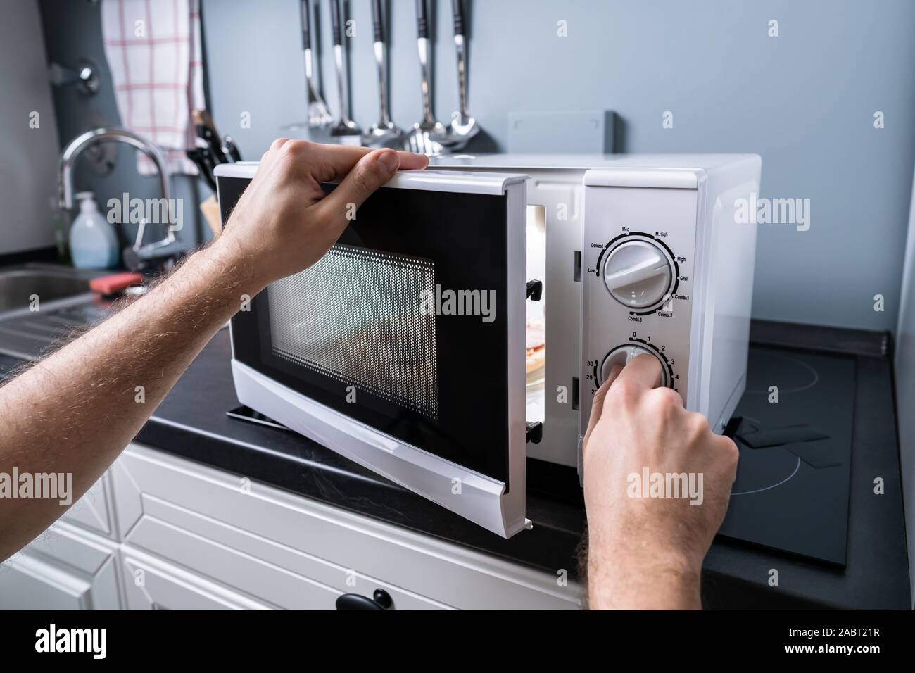 Young Man Preparing Food In Microwave Oven On Kitchen Counter Stock Photo