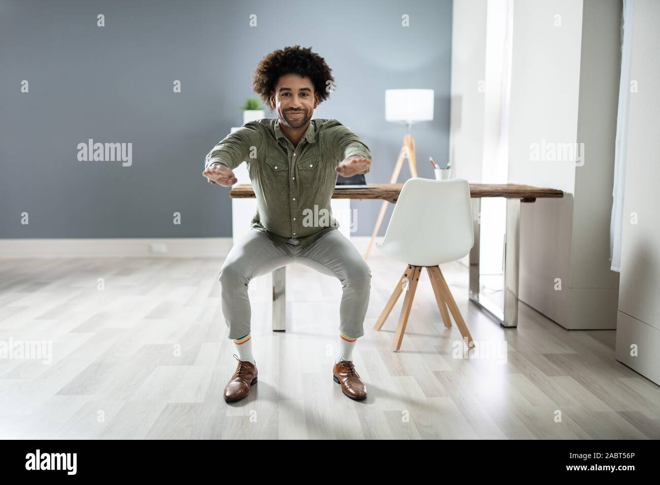 Smiling Young Businessman Doing Sit-ups At Workplace Stock Photo