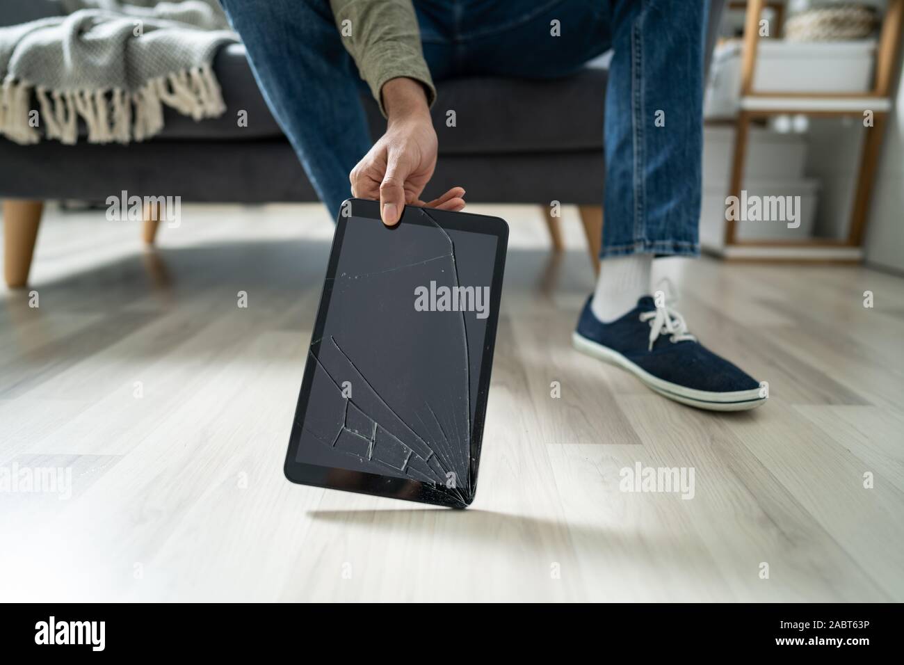 Man's Hand Picking Up Tablet With Broken Screen Stock Photo