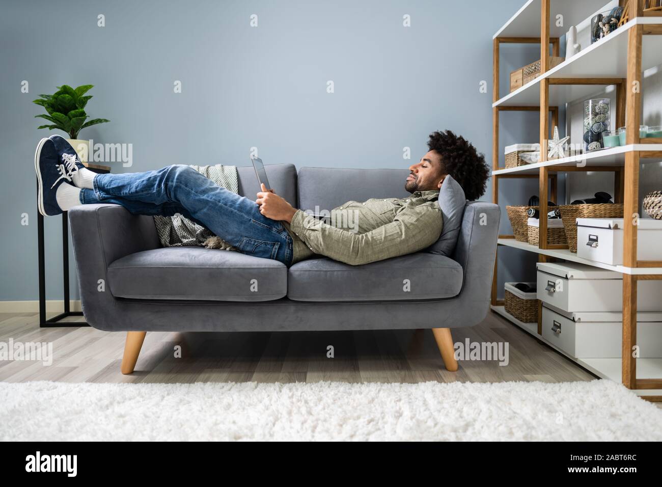 Man Using Digital Tablet Lying In Sofa Stock Photo