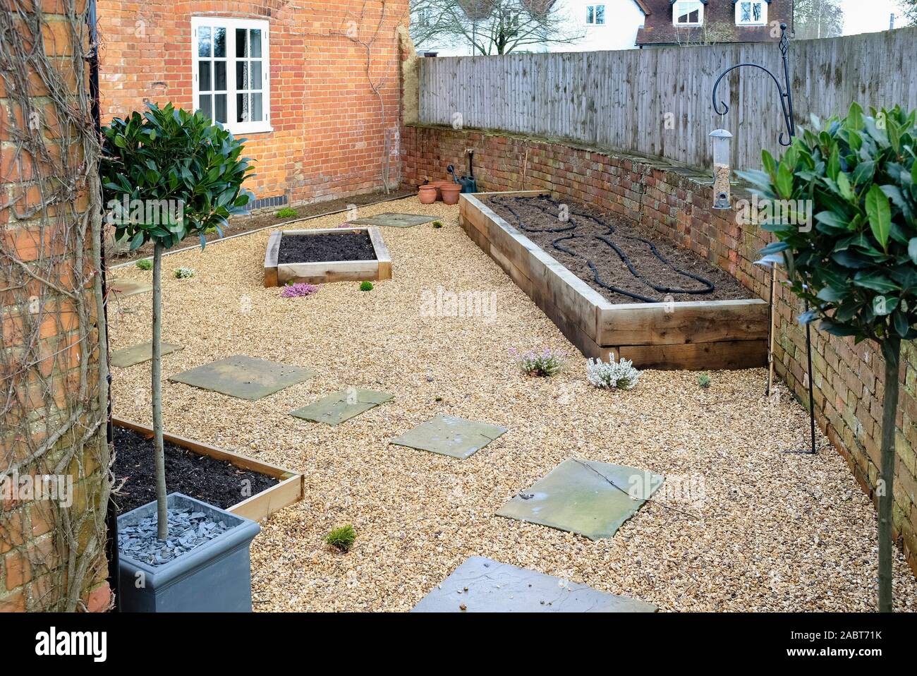 Small garden design with hard landscaping, gravel and york stone path, oak sleeper raised beds and bay trees Stock Photo