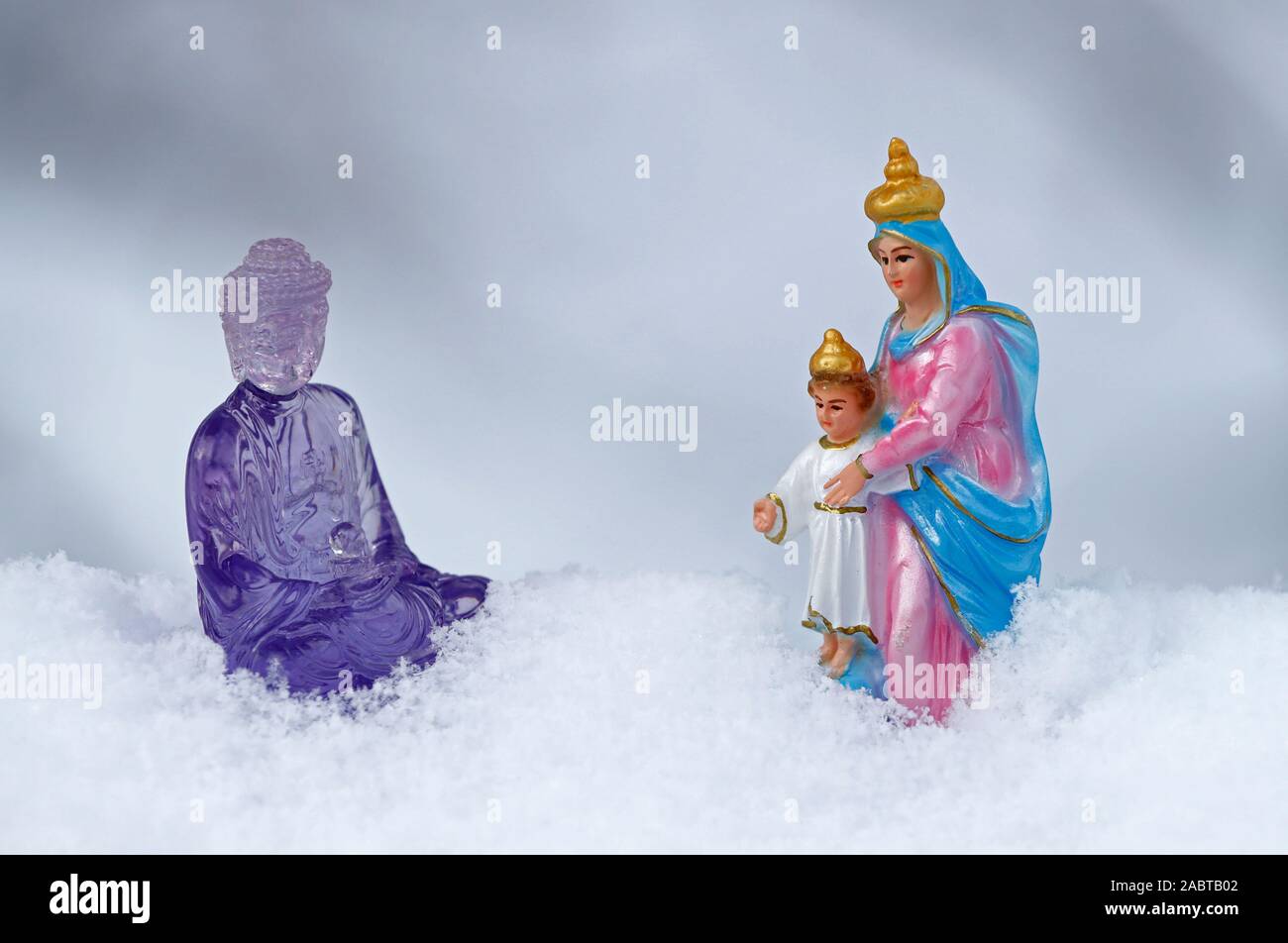 Purple plastic buddha  and Virgin Mary statues in the snow.  France. Stock Photo