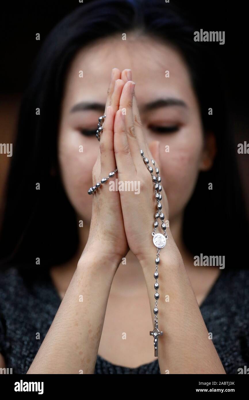 Hands of a woman holding a rosary or crucifix while praying, Christian daily devotional of a worshiper of God the Savior.  Hue.  Vietnam. Stock Photo