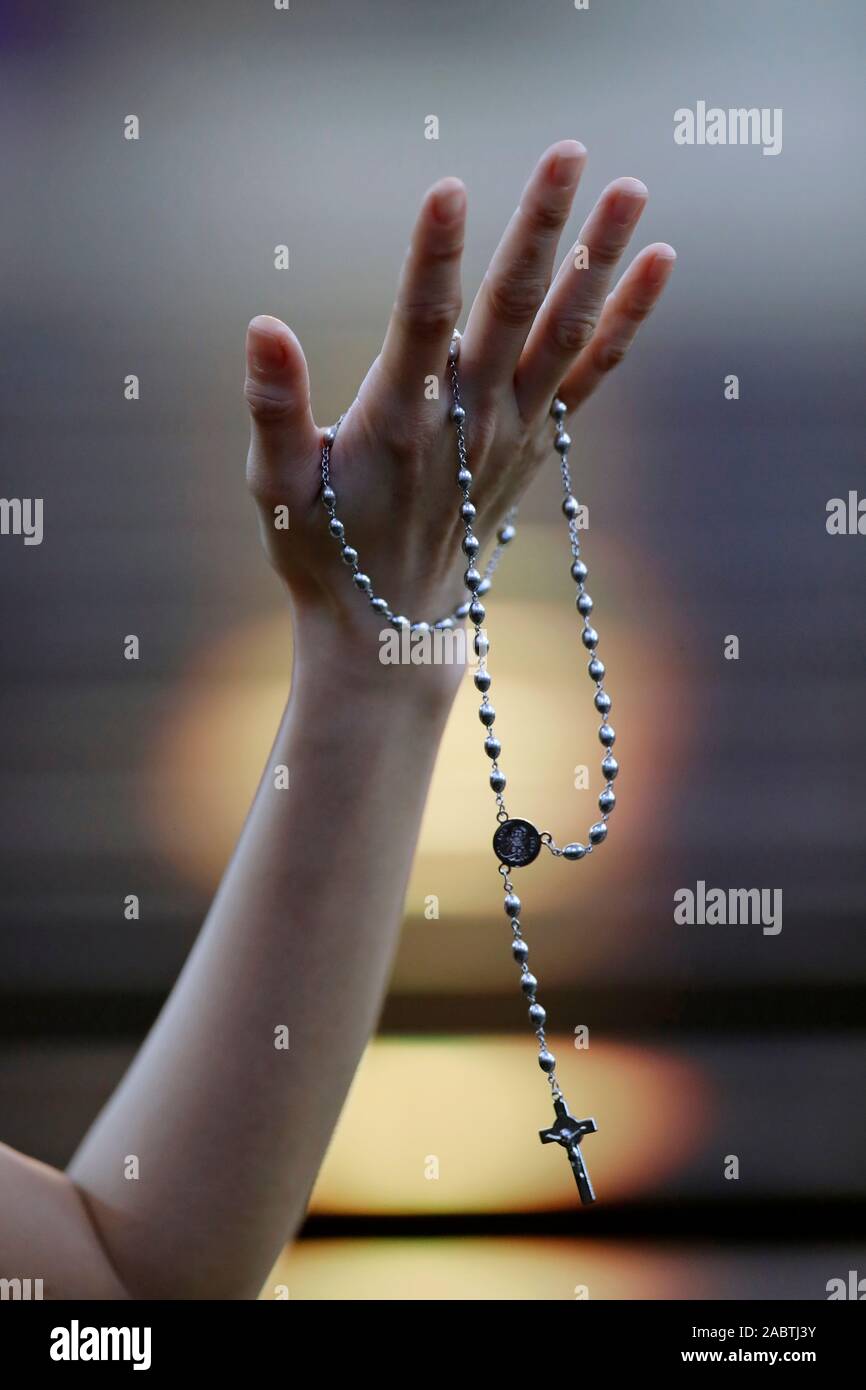 Hand of a woman holding a rosary or crucifix while praying, Christian daily devotional of a worshiper of God the Savior.  Hue.  Vietnam. Stock Photo