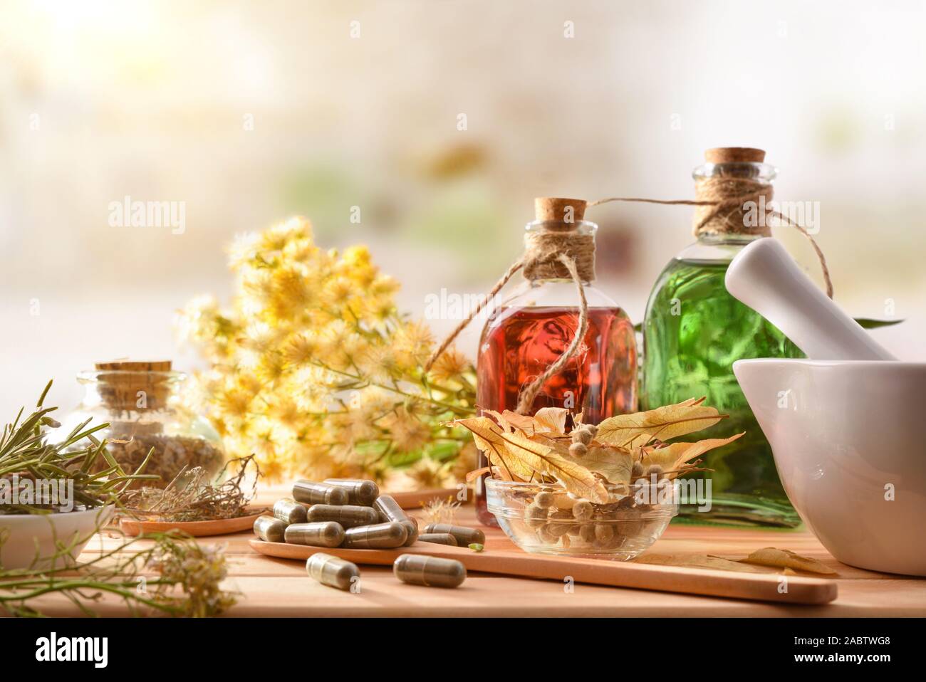 Capsules and bottles of essence of natural medicine with medicinal plants on wooden table in rustic kitchen. Front view. Horizontal composition. Stock Photo