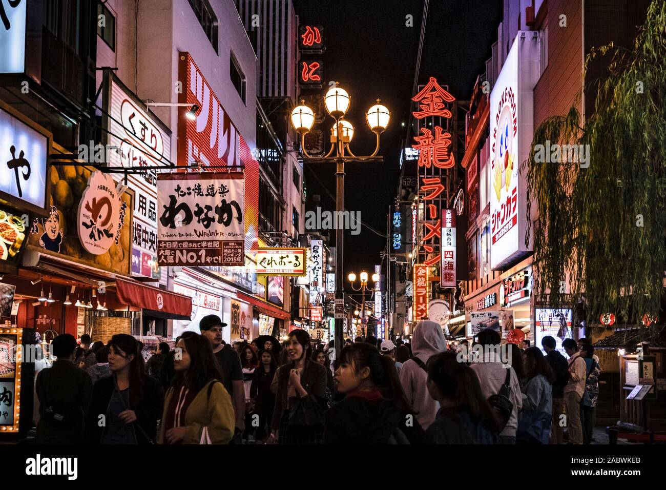 Crowd of tourists strolling down one of the streets in Osaka's Dotonbori area. Cityscape by night with lots of billboards and lights. Stock Photo