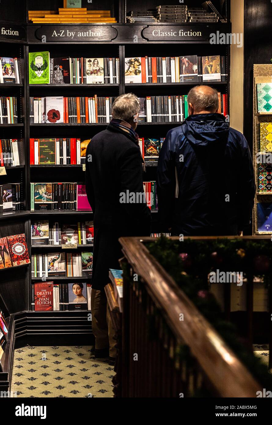 Rear view portrait of two men standing side by side in front of a 'classic fiction' bookshelf, Hatchards bookshop, London, England, UK. Stock Photo