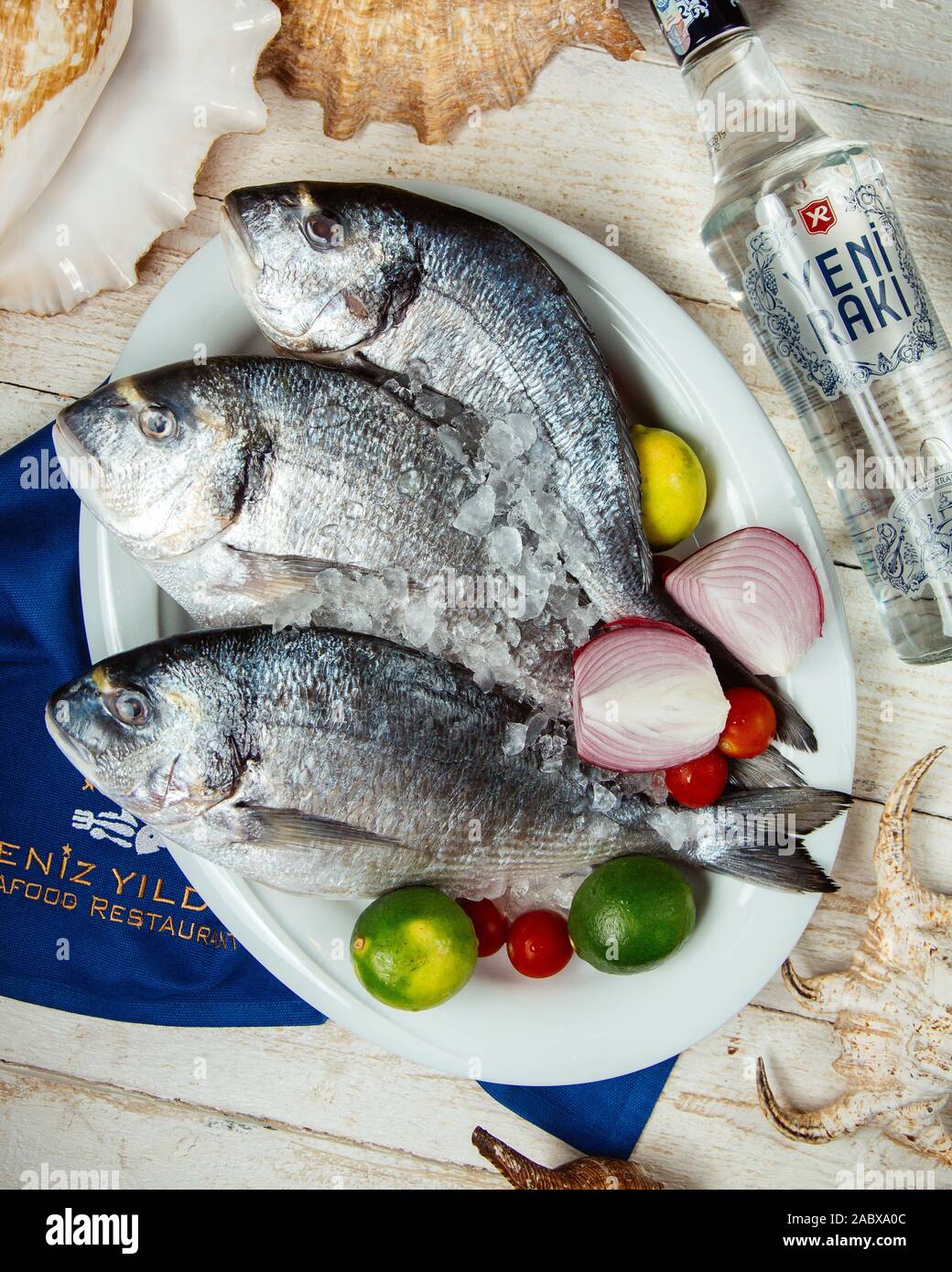 top view of fresh fish served with lemon, onions and tomatoes and raki bottle Stock Photo