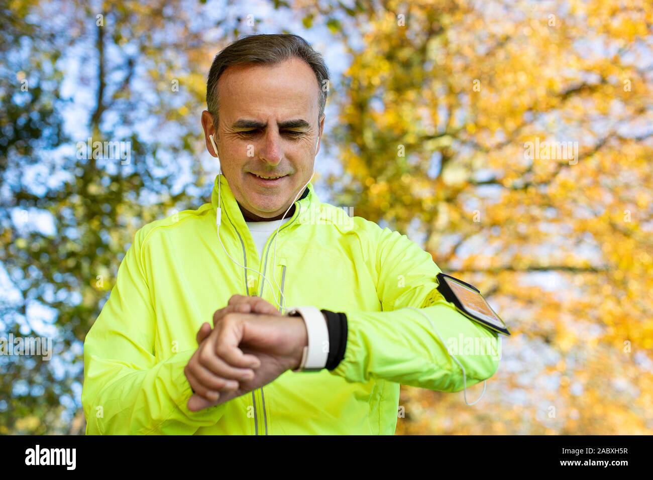 Mature Man Exercising In Autumn Woodland Looking At Activity Tracker On Smart Watch Stock Photo