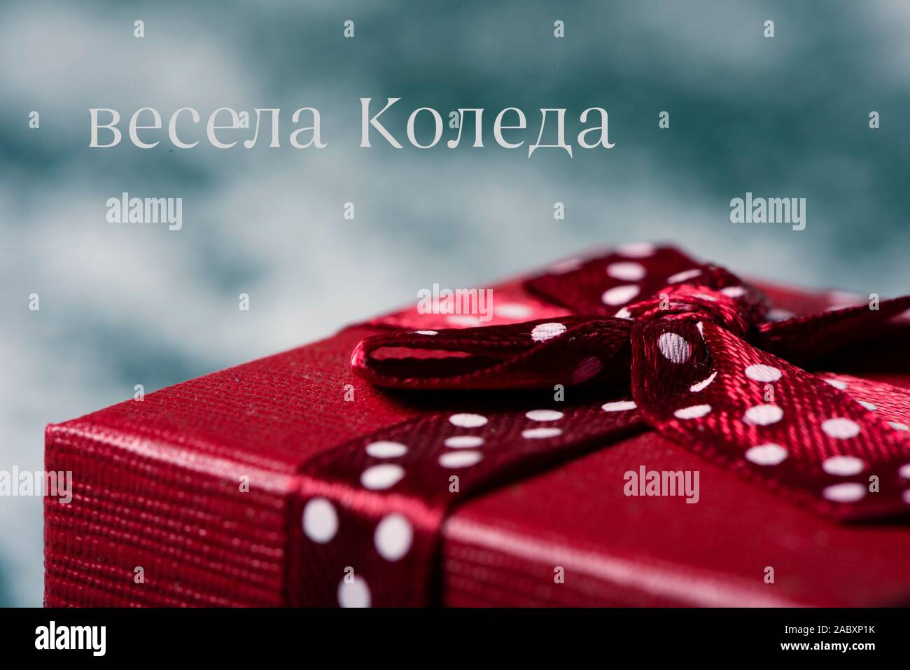 closeup of a red gift box, tied with a nice red ribbon, on the snow and the text merry christmas written in bulgarian Stock Photo