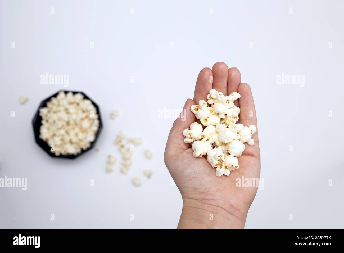 Person holding popcorn in hand top view, with popcorn in bowl isolated on white background Stock Photo