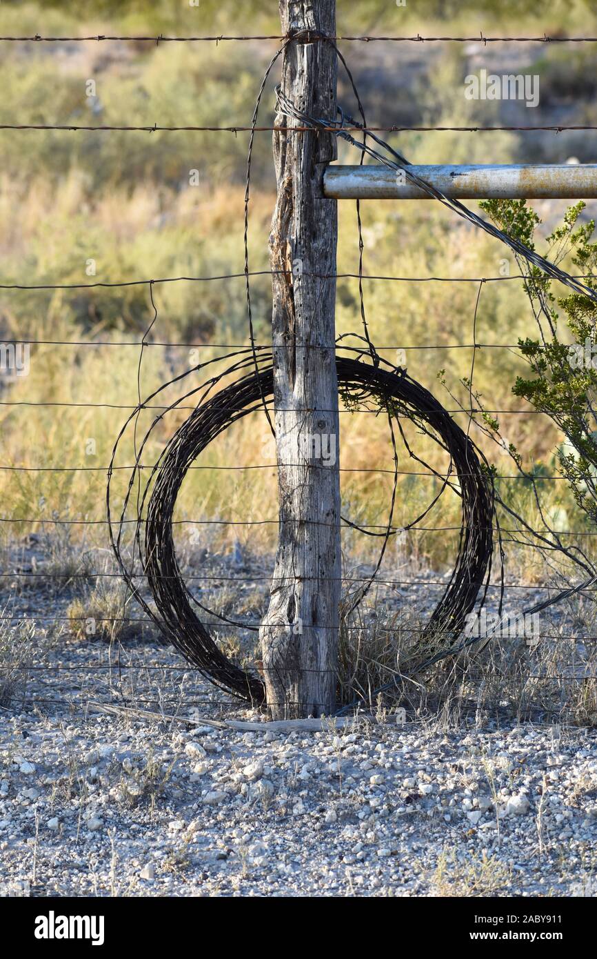 Roll of barbed wire leaning against a primitive tree branch fence post in the old west Stock Photo