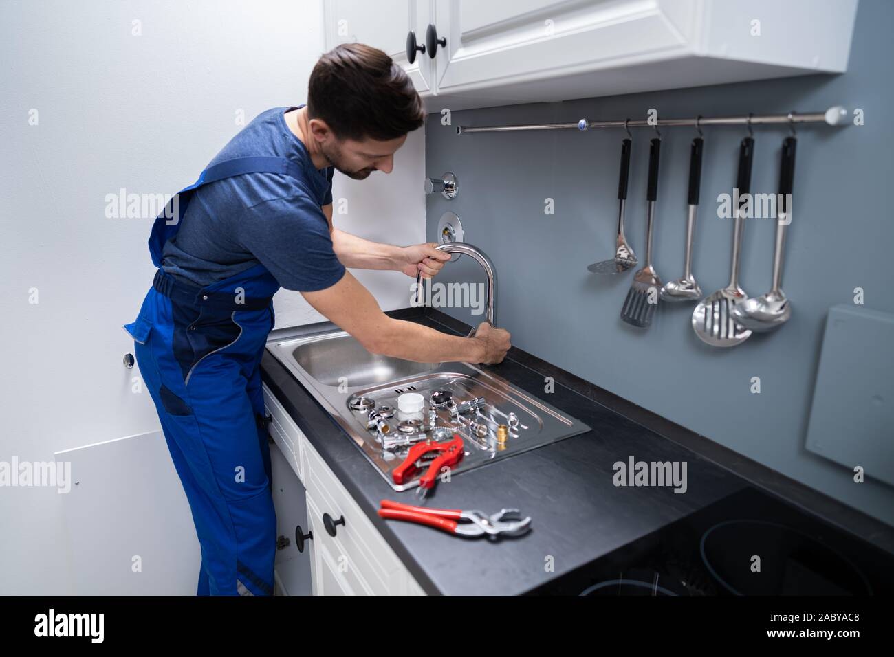 Happy Young Male Plumber Fixing Faucet In Kitchen Stock Photo