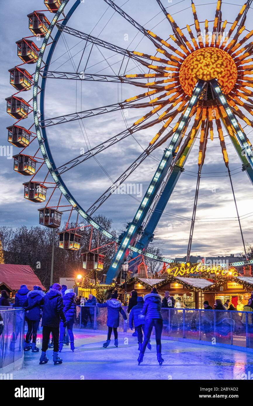 Skaters skate on ice skating rink in front of ferris wheel at the