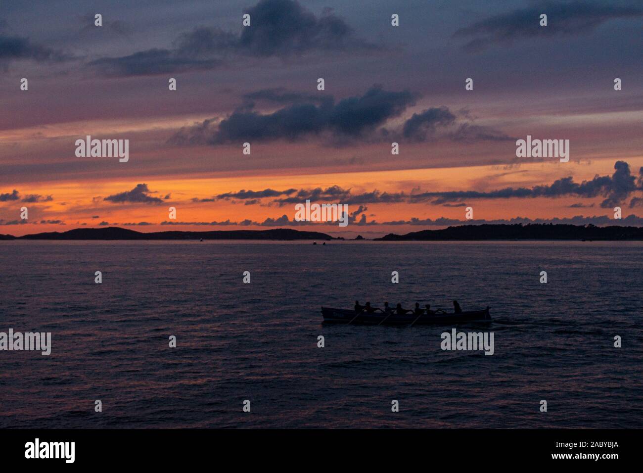 A Cornish pilot gig boat being rowed between the Isles of Scilly at sunset Stock Photo