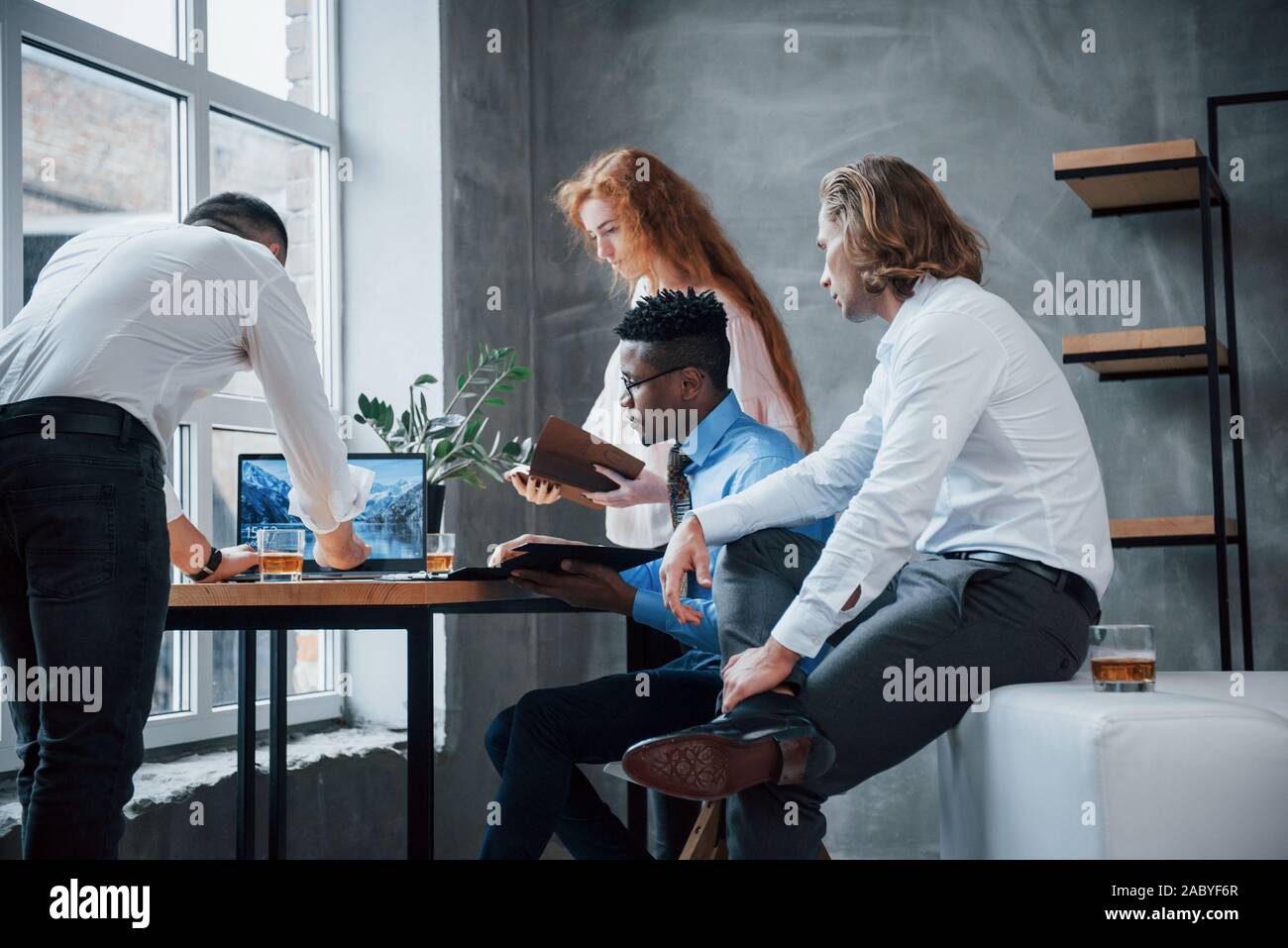 Using laptop. Group of multiracial office workers in formal clothes talking about tasks and plans Stock Photo