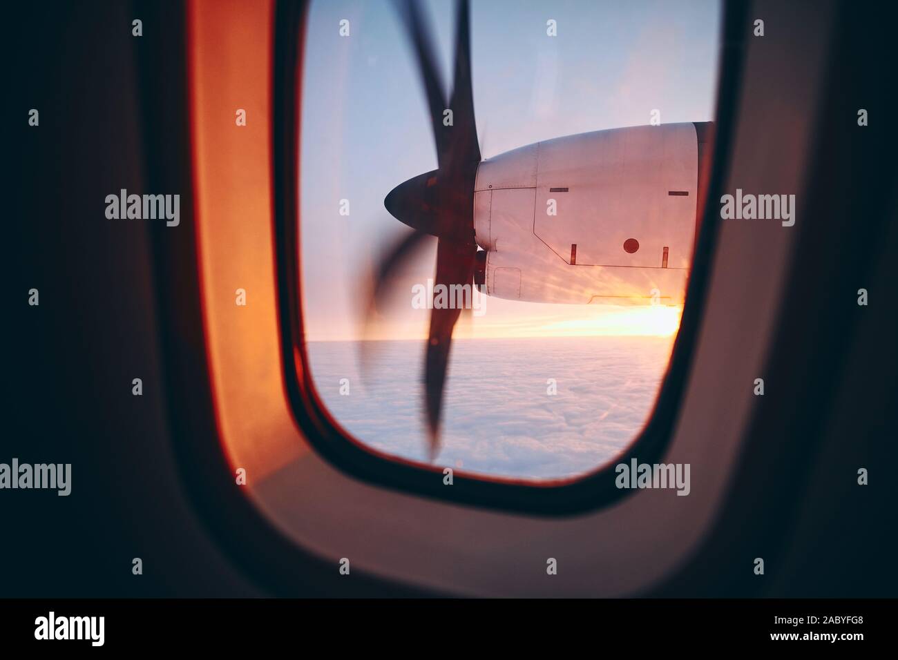 View from window of propeller airplane during flight above clouds at beautiful sunrice. Selective focus on turboprop engine. Stock Photo