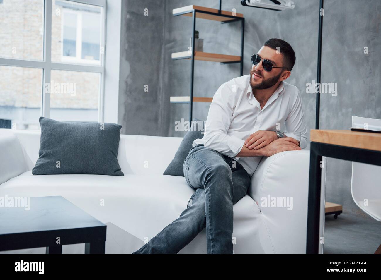 Young short-haired man in sunglasses sitting on couch in the office Stock Photo