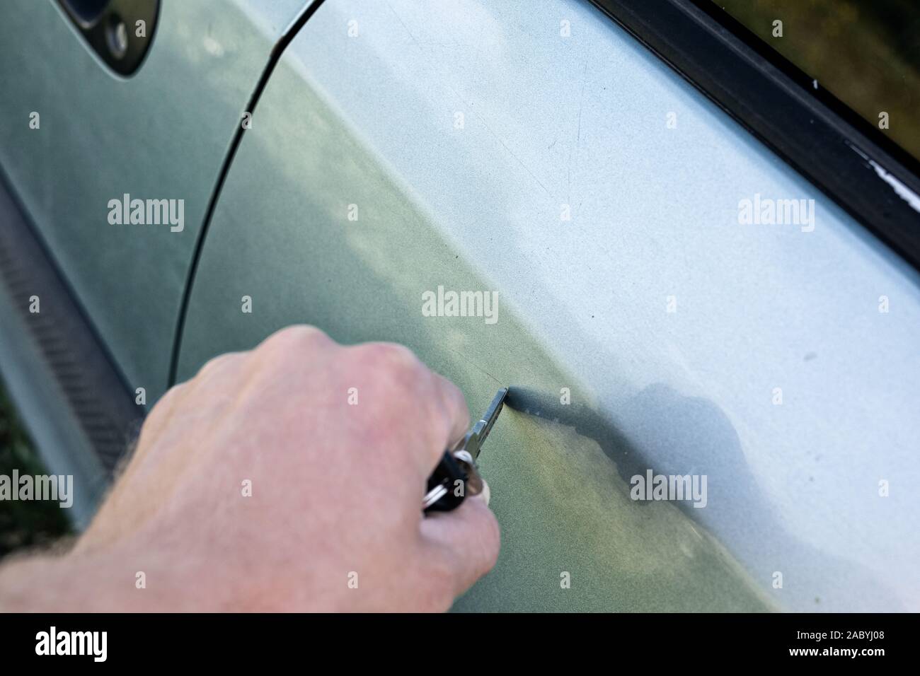 male hand scratches car wing with a key Stock Photo